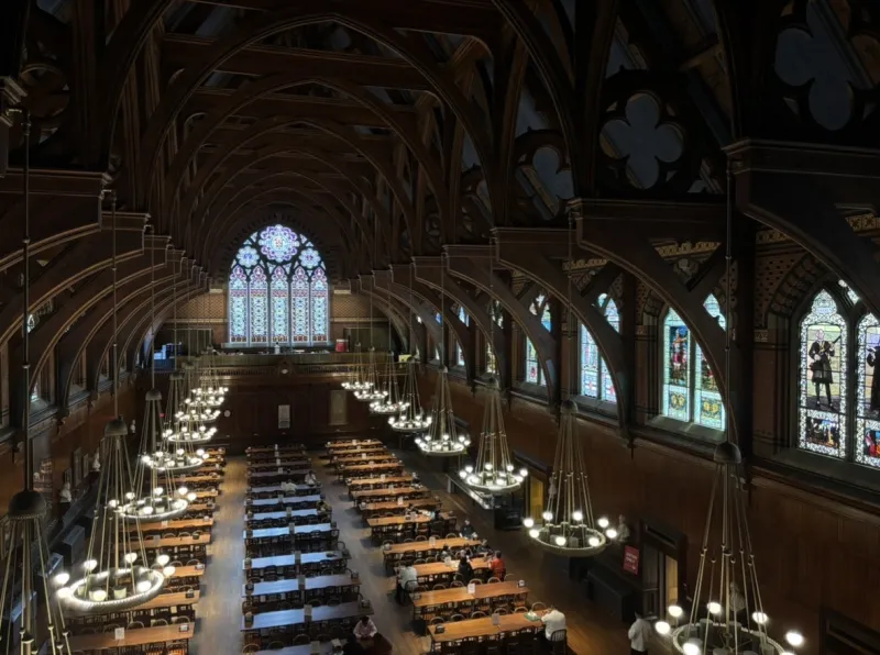 Large dining hall with rows of wood tables, chandeliers, and stained glass windows