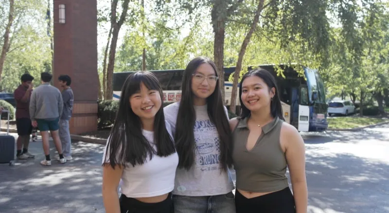 Three girls standing together with trees in the background