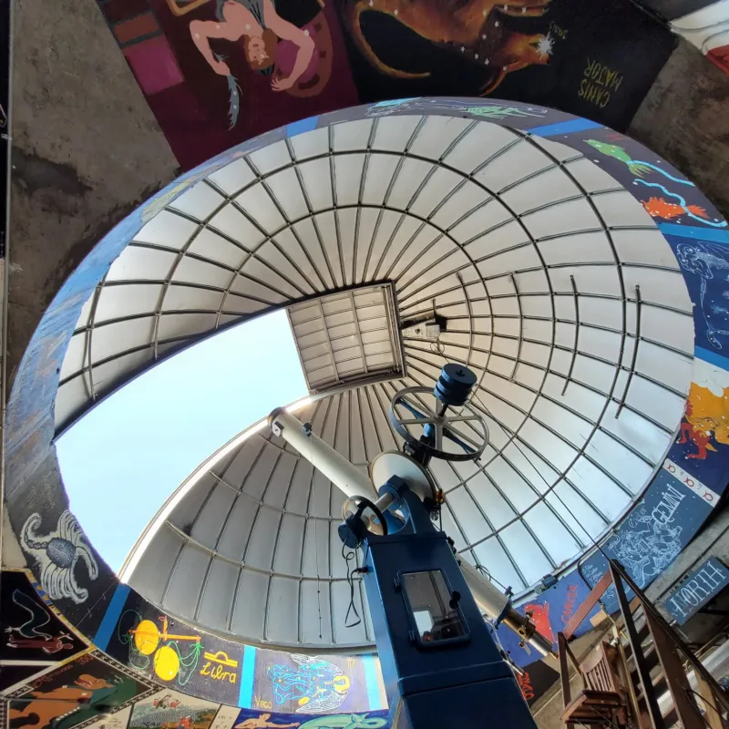 A dome with a telescope, seen from inside below the telescope. The rim of the dome has paintings of constellations around it.