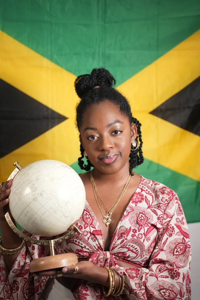 Zaria Ferguson '26 holding a globe against a Jamacian flag.