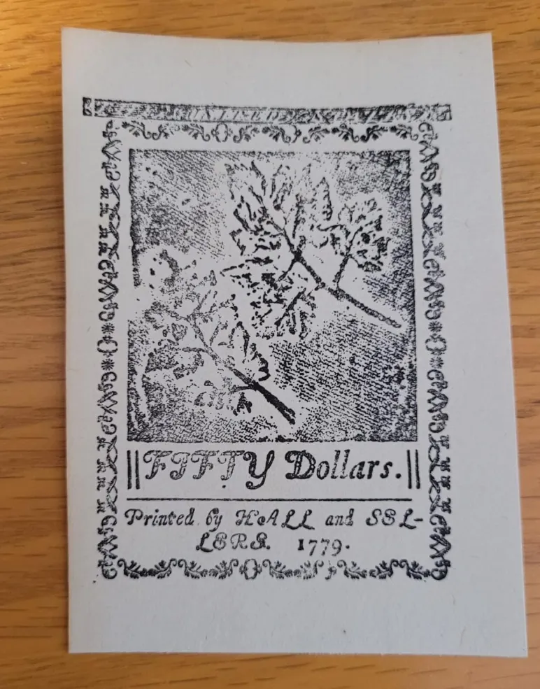 a small paper rectangle printed with a design of two leaves. At the bottom it reads, "fifty dollars." It also has the year 1779.
