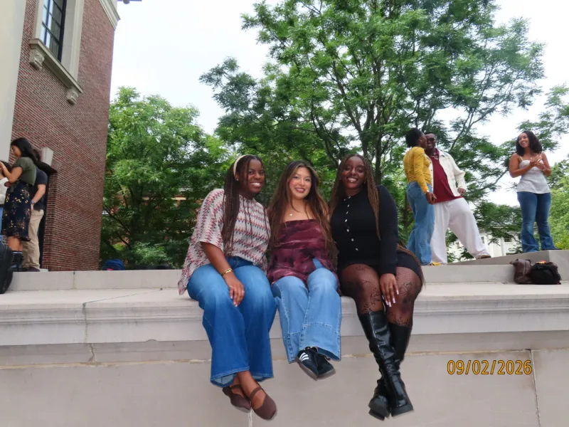 Three friends sitting on the ledge in front of Widener Library. 
