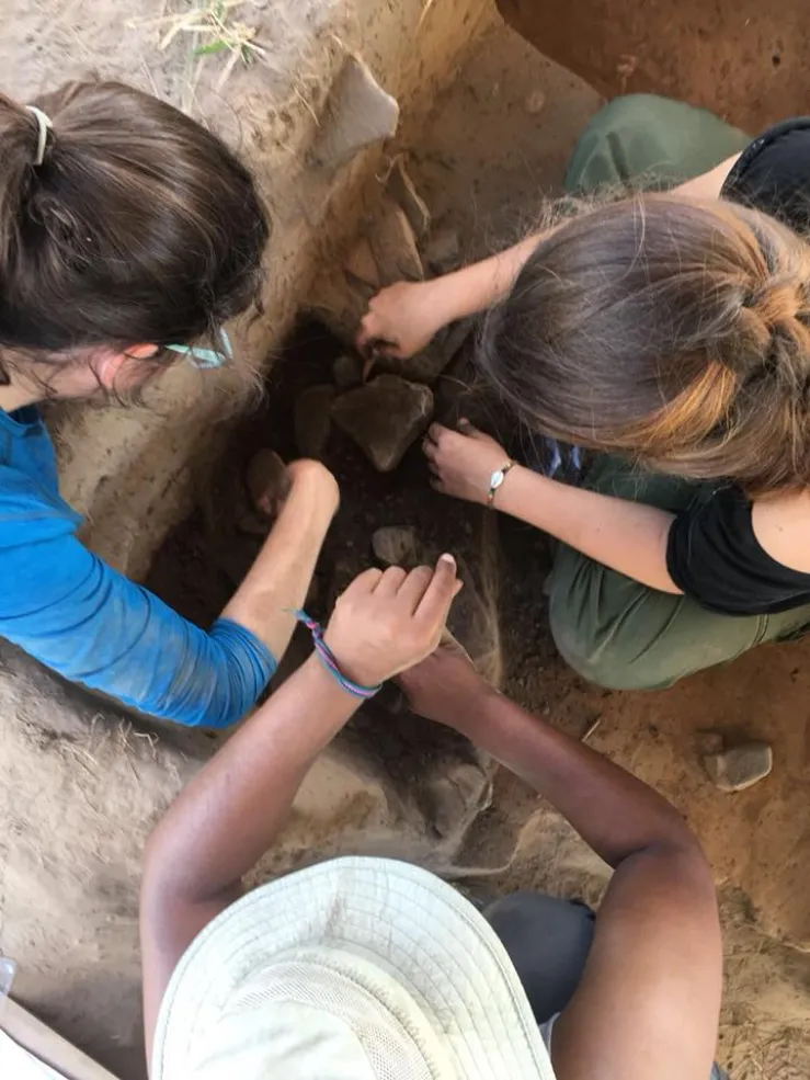 three students working in an excavation unit