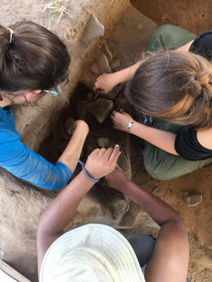 three students working in an excavation unit