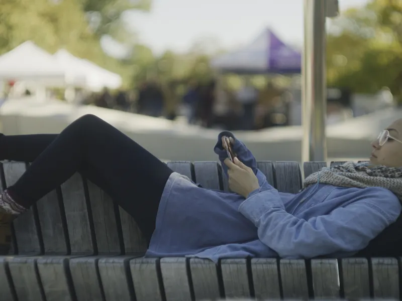 Student laying on bench at Science Center Plaza with her phone