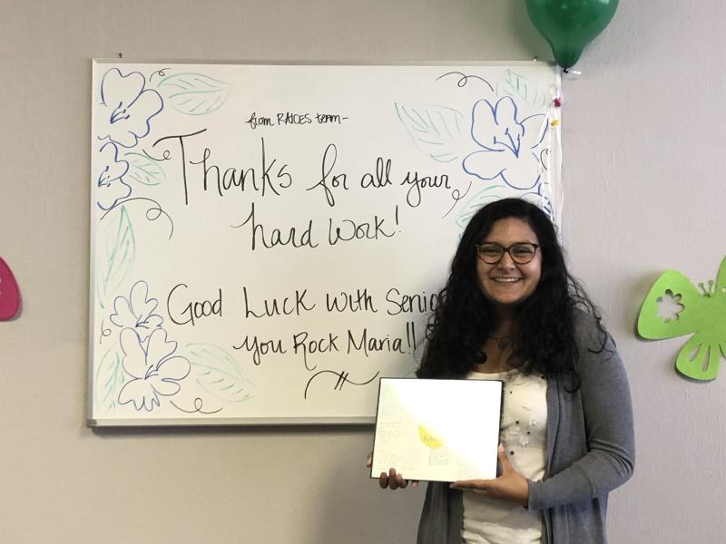 Maria posing in front of a farewell message at the end of her internship. 