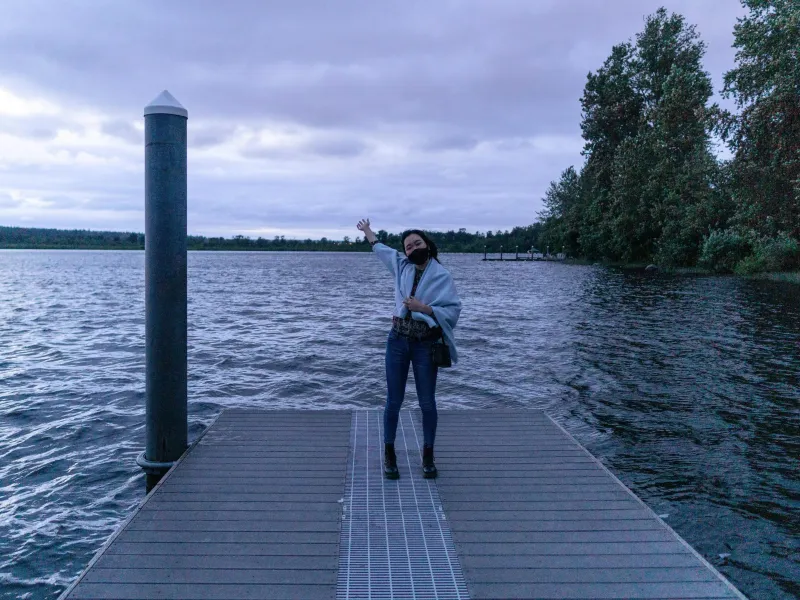 I am posing happily by a lake in my hometown near Seattle, WA. It's really cloudy and getting dark. 