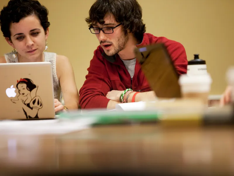 Two students sharing a laptop and speaking to one another