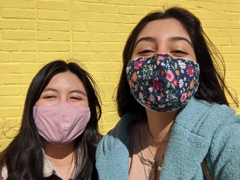 Two girls standing in front of a yellow wall.