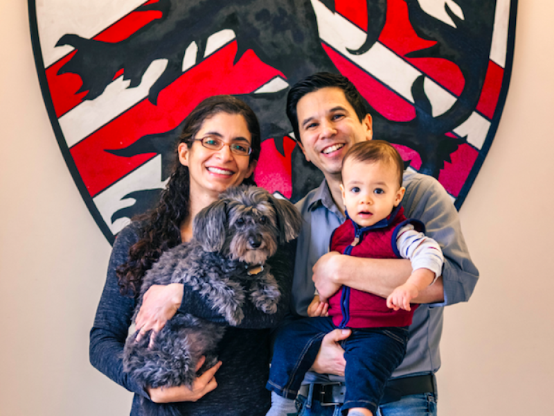 A portrait of Kiran Gajwani and Stephen Chong, faculty deans of Winthrop House, with their son and dog.