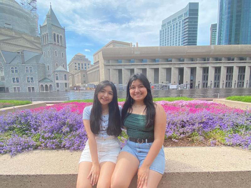 Two girls sitting by flower beds.