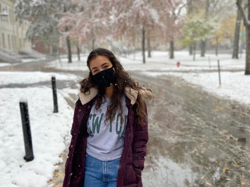 Girl in a big dark red coat in a park while it is snowing. 