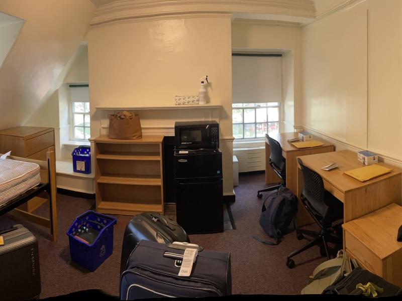 Picture of a dorm room with luggage and unorganized furniture.