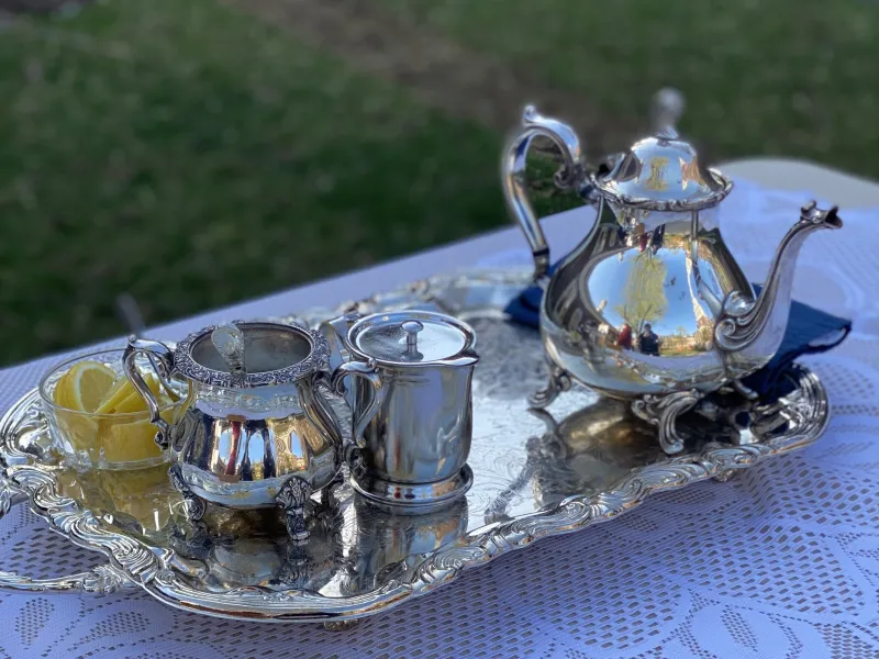 A picture of a silver teapot, creamer pitcher, sugar container, and bowl of lemons on a silver platter.
