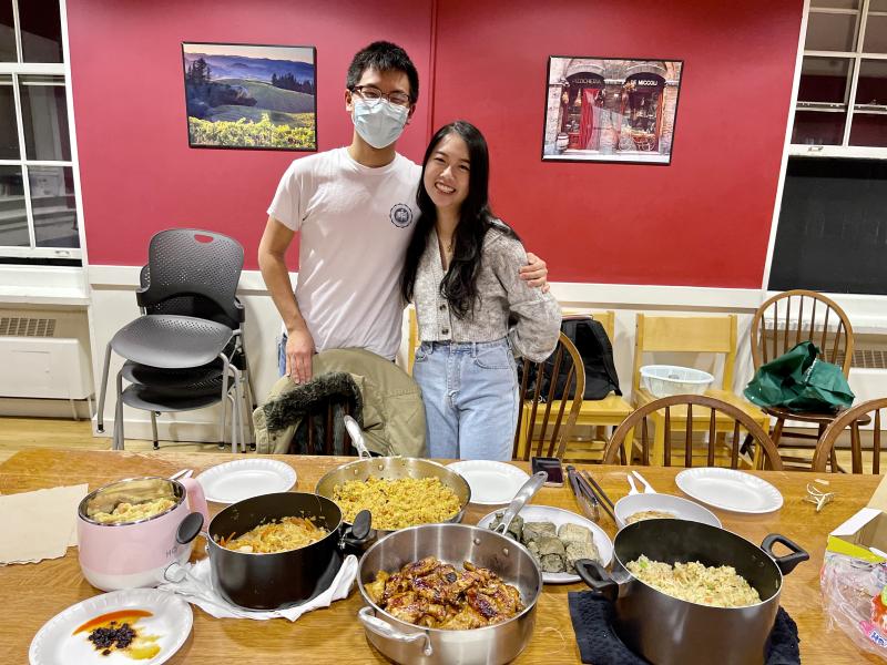 Janny and Raymond standing in front of a table covered in plates and pots with food.