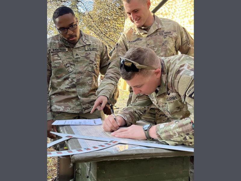 Three men look at papers on a table, including Henry Sullivan Atkins '20