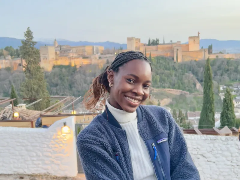 Writer smiling in front of Granada's Alhambra, a castle-like structure on the horizon.