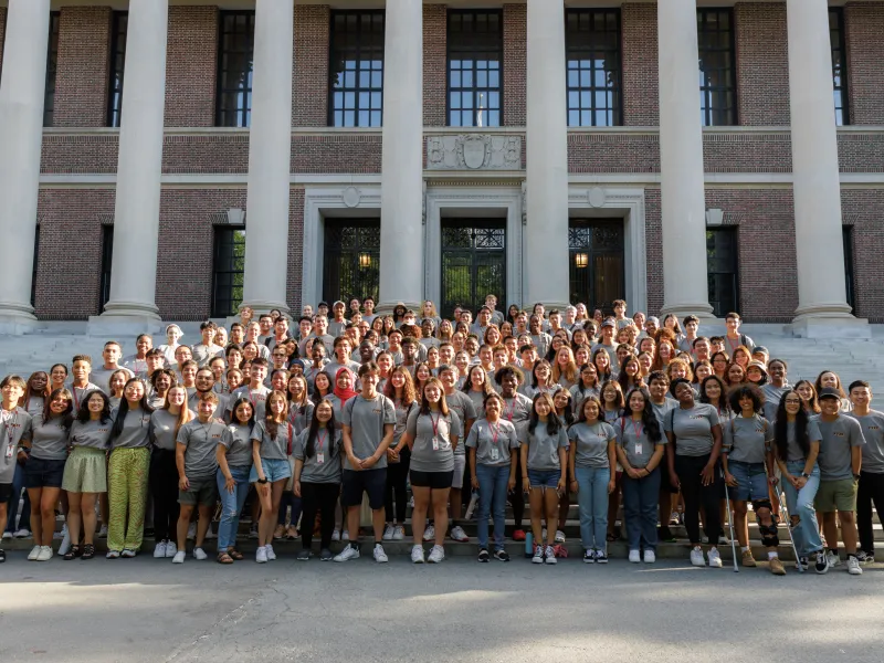 A large group of students gather in front of a library to pose for a picture. 