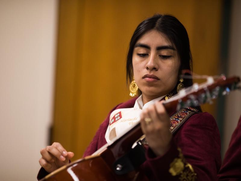 A female mariachi musician holds her instrument while wearing her mariachi suit