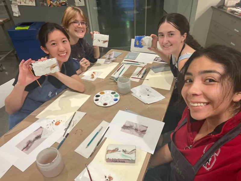 Four students smiling and surrounding a table with artworks