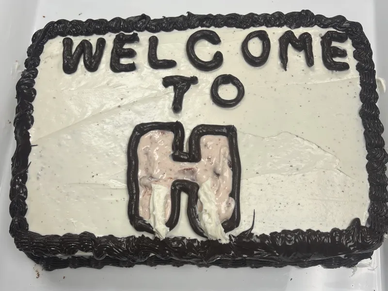 Image of a cake with white and black frosting and the words “Welcome to H” written on top.