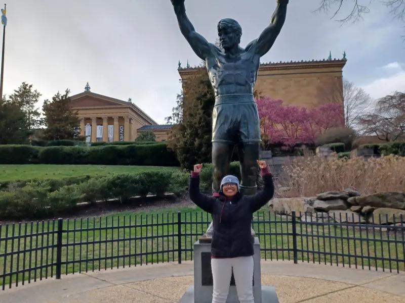 Merlin standing in front of Rocky Statue with fists in the area in front of the steps where the Rocky movie scene was shot