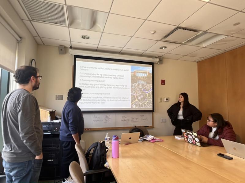 Students sitting and standing around a table looking at a presentation