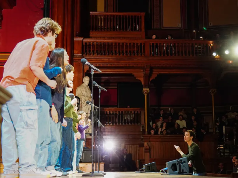 Performers on stage with microphones, while an audience watches.