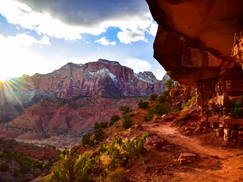 A picture of the Watchman Trail with the setting sun and snow-capped mountains in the background.