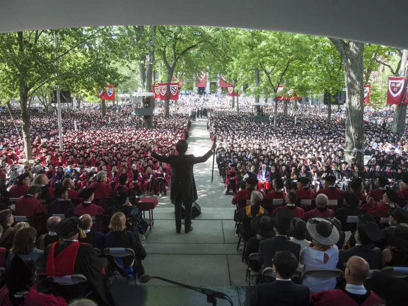 Speaker addressing a large crowd at an outdoor graduation ceremony