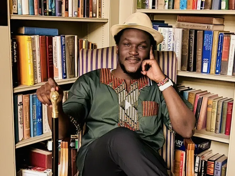 Photo of David sitting amongst some bookcases filled with books