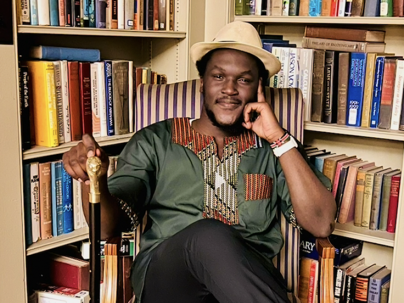 Photo of David sitting amongst some bookcases filled with books