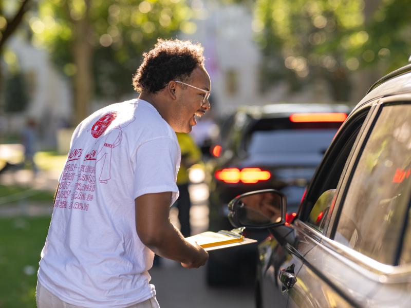 A Harvard student smiles at a car and helps the passengers with directions while entering Harvard Yard on move-in day.
