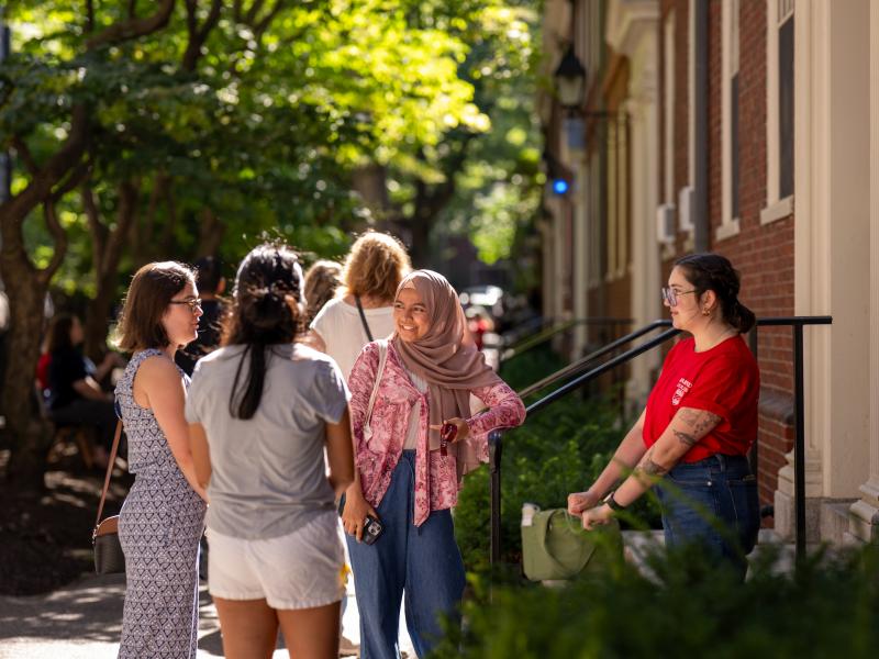 A group of female students smile and talk to each other outside one of the Harvard residence halls.