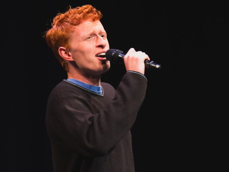 Person singing into a microphone on stage.