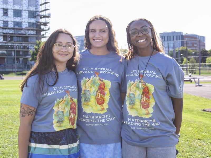 Three Harvard College students smile together while wearing Powwow 2025 t-shirts.