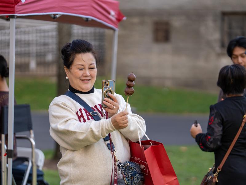 A woman in a white Harvard sweatshirt takes a picture of her chocolate covered strawberries on a stick.