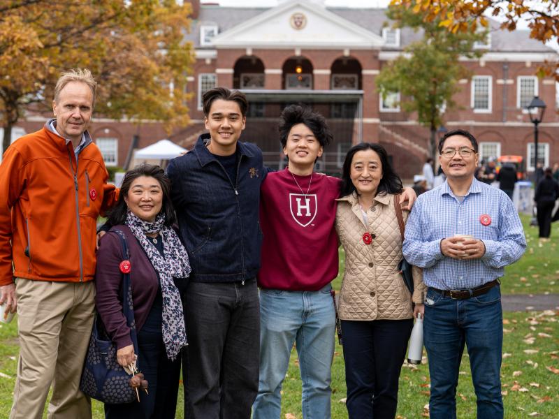 A family of six smiles for a photo together while wearing Harvard merchandise.