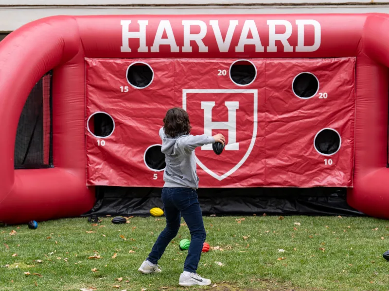 A young boy throws a football into a inflatable red Harvard football toss board.