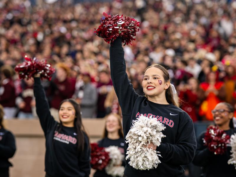 Harvard cheerleaders lifting their pom poms in the air during a cheer.