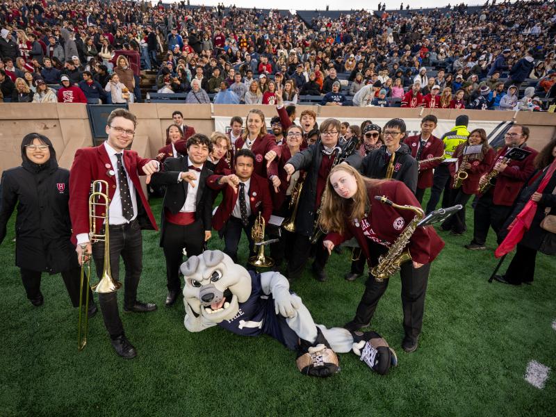 The Harvard band takes a picture with the Yale Bulldog mascot on the sideline.
