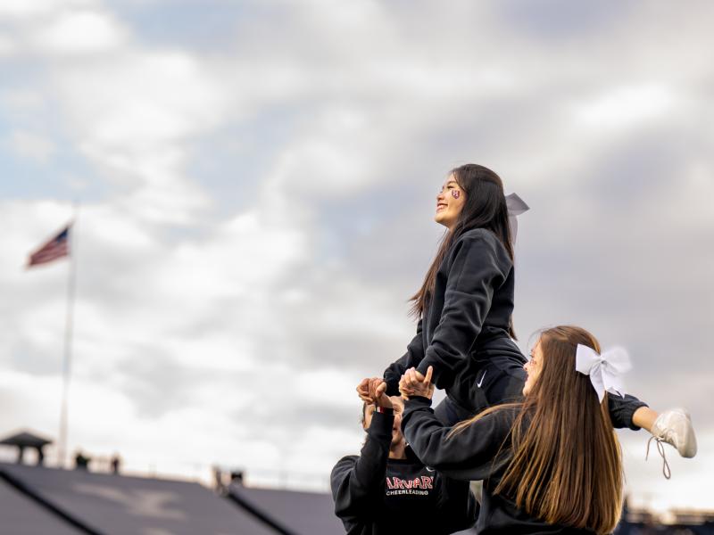 A Harvard cheerleader is lifted to the top of the pyramid with her teammates holding her up.