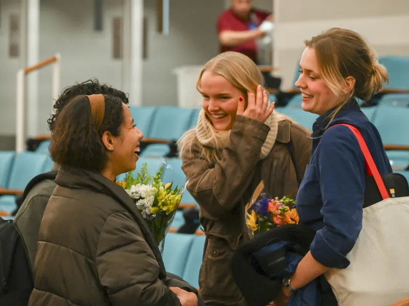 A group of three female students smile while talking to each other after the program.