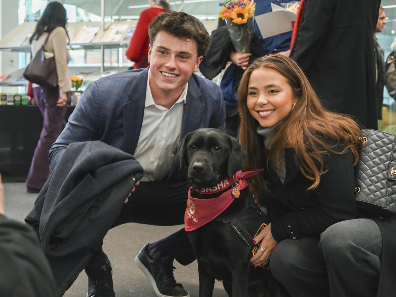Two students smiling with Sasha, the campus' community engagement dog.