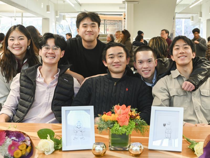 A group of students smile next to a table of flowers at the reception.