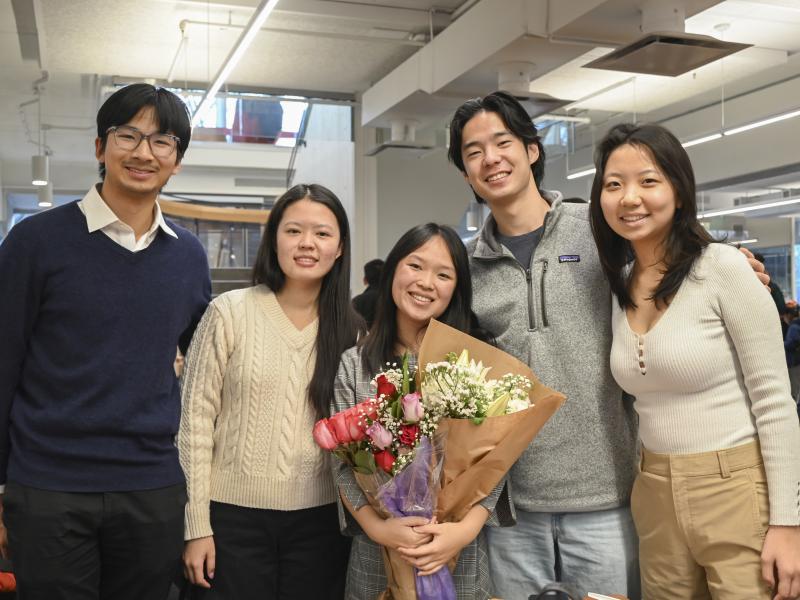 A graduating female student holds a big bouqet of flowers while smiling next to her friends.