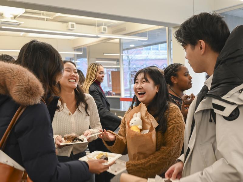 A young female student smiles at her friend while they enjoy dessert at the reception.