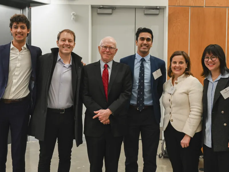 Three faculty members, the College Dean, and two students smile together. 