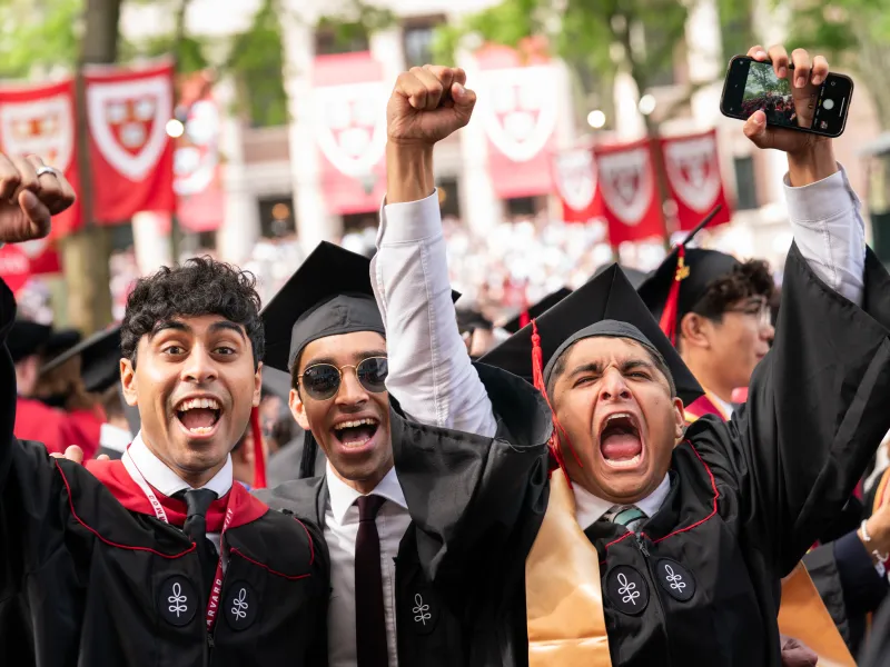 Three male students cheer with expressive faces during Commencement.