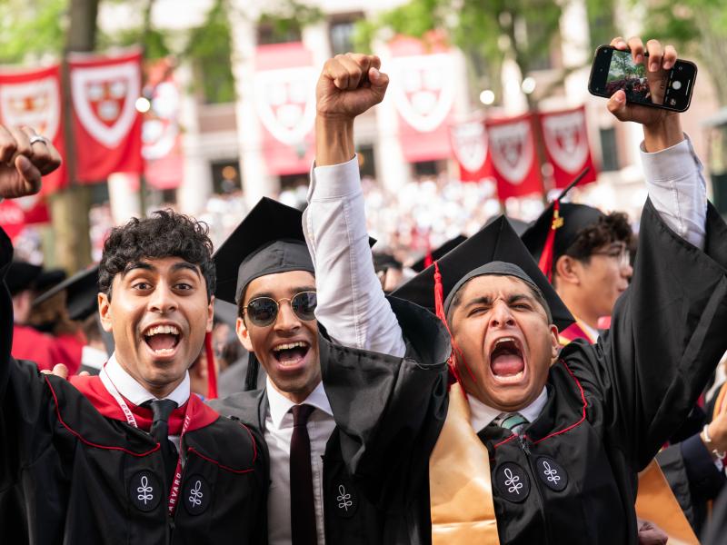 Three male students cheer with expressive faces during Commencement.